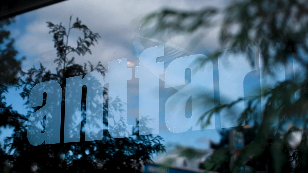 Close-up image of the AntFarm logo on a window that also shows a reflection of trees